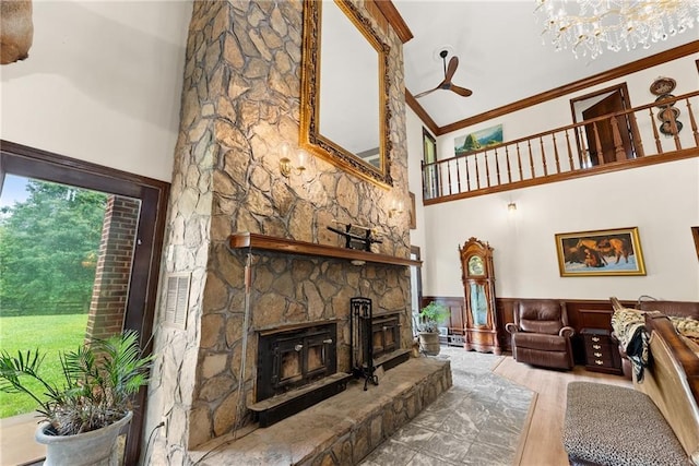 living room with a wainscoted wall, wood finished floors, a high ceiling, crown molding, and a stone fireplace