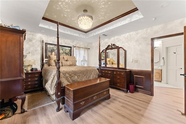 bedroom featuring a wainscoted wall, a tray ceiling, crown molding, and light wood-style floors