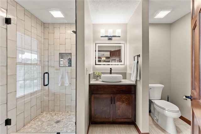 full bath with toilet, a stall shower, vanity, a textured ceiling, and baseboards