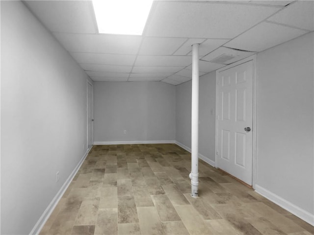 finished basement with a paneled ceiling, light wood finished floors, and baseboards