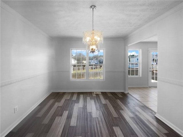 unfurnished dining area with baseboards, ornamental molding, wood finished floors, and an inviting chandelier