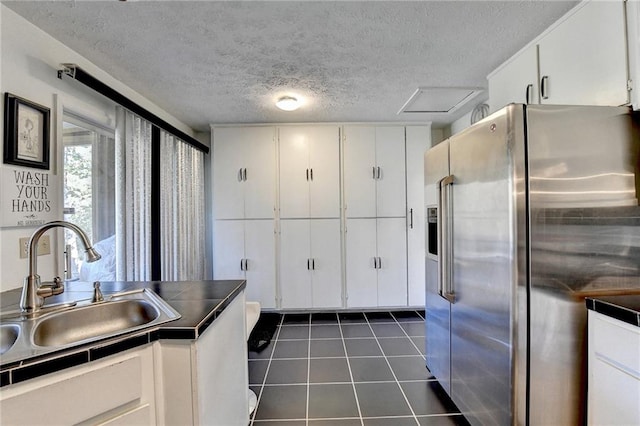 kitchen with sink, a textured ceiling, high quality fridge, white cabinets, and dark tile patterned flooring