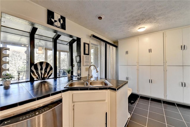 kitchen featuring white cabinetry, sink, stainless steel dishwasher, tile countertops, and a textured ceiling