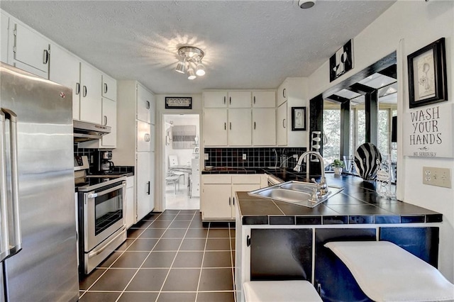 kitchen with white cabinets, sink, decorative backsplash, appliances with stainless steel finishes, and kitchen peninsula