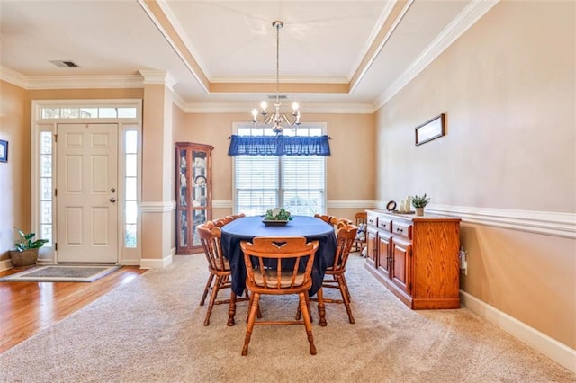 dining space with a notable chandelier, crown molding, light colored carpet, and a raised ceiling