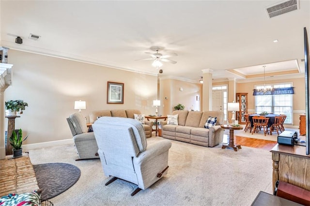 living room with a tray ceiling, ceiling fan with notable chandelier, ornamental molding, and decorative columns