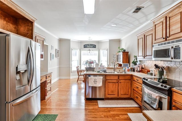 kitchen with pendant lighting, sink, light wood-type flooring, and appliances with stainless steel finishes