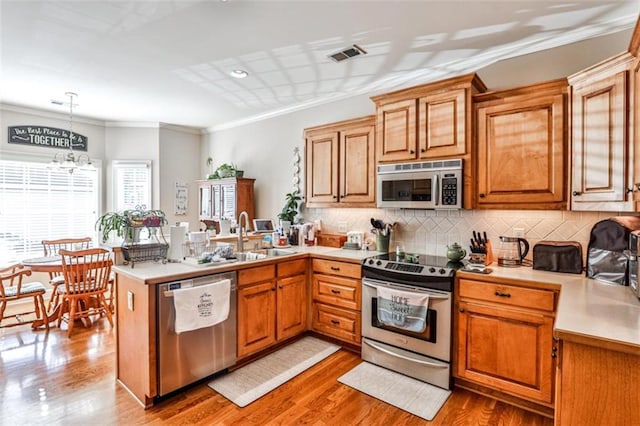 kitchen with sink, decorative light fixtures, kitchen peninsula, stainless steel appliances, and backsplash