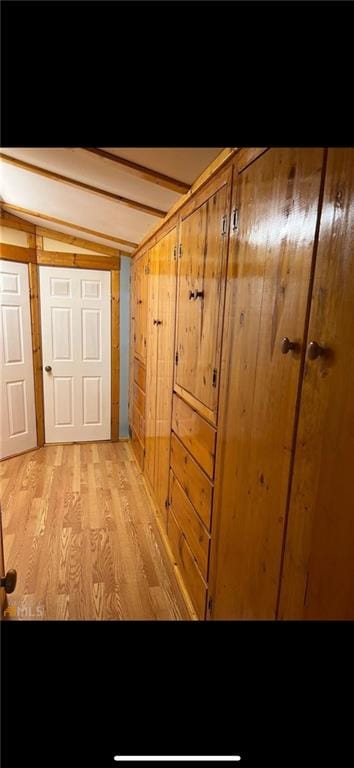 hall featuring light wood-type flooring, vaulted ceiling with beams, and wooden walls