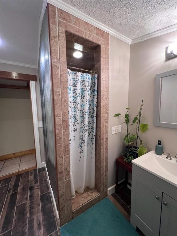 bathroom featuring a textured ceiling, ornamental molding, vanity, and curtained shower