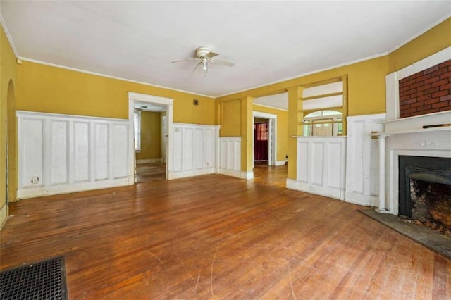 unfurnished living room with hardwood / wood-style flooring, crown molding, ceiling fan, and a brick fireplace