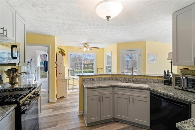 kitchen featuring black appliances, a peninsula, a sink, and gray cabinetry