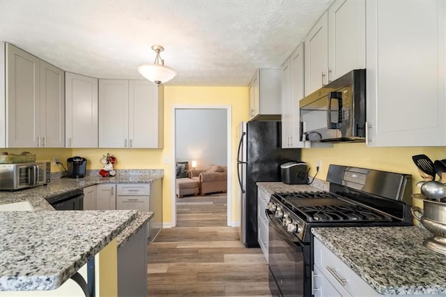 kitchen with light wood finished floors, a toaster, baseboards, light stone counters, and black appliances