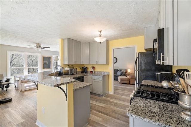 kitchen with light wood-style flooring, a peninsula, a kitchen bar, and light stone countertops