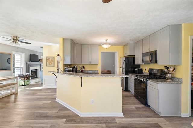 kitchen featuring a fireplace with raised hearth, light wood-style flooring, light stone countertops, a peninsula, and black appliances