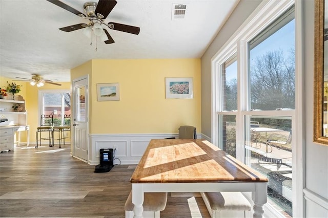 dining room featuring dark wood-style flooring, visible vents, a decorative wall, and wainscoting