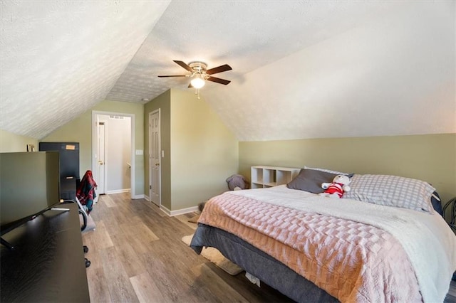 bedroom with a ceiling fan, vaulted ceiling, a textured ceiling, wood finished floors, and baseboards