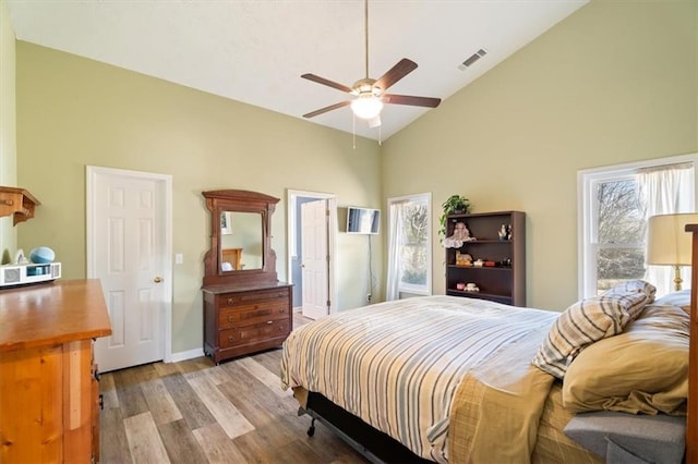 bedroom with high vaulted ceiling, light wood-style flooring, multiple windows, and visible vents