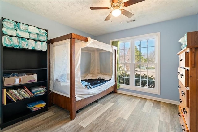 bedroom with visible vents, a ceiling fan, a textured ceiling, wood finished floors, and baseboards