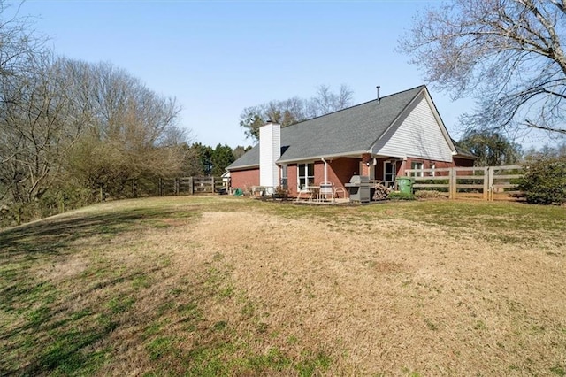 rear view of property featuring brick siding, a chimney, fence, and a lawn