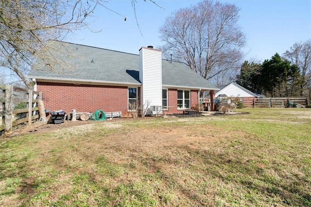 back of property featuring brick siding, fence, a chimney, and a lawn