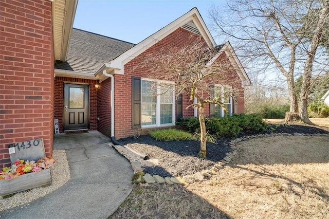 view of exterior entry with a shingled roof and brick siding