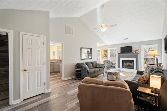 living room featuring baseboards, visible vents, a fireplace with raised hearth, a ceiling fan, and light wood-style floors