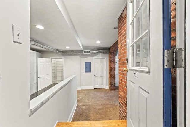 hall featuring baseboards, concrete floors, visible vents, brick wall, and electric panel