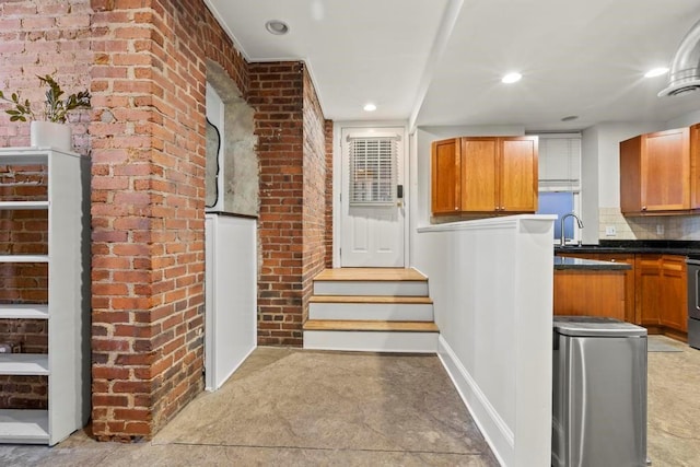 kitchen with decorative backsplash, dark countertops, brick wall, and a sink