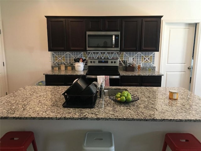 kitchen with a kitchen breakfast bar, tasteful backsplash, light stone counters, and stainless steel appliances