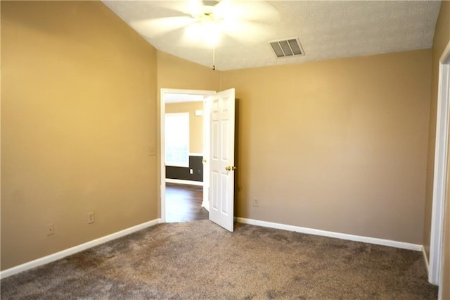 spare room with vaulted ceiling, ceiling fan, and dark colored carpet