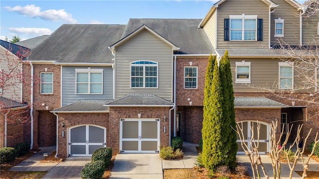 townhome / multi-family property featuring an attached garage, brick siding, driveway, and roof with shingles