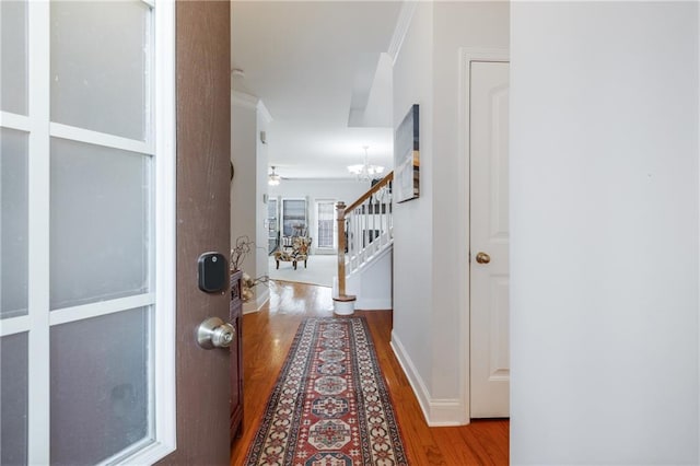 hall with wood finished floors, an inviting chandelier, crown molding, baseboards, and stairs