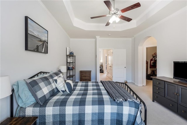 bedroom with ornamental molding, a tray ceiling, arched walkways, light colored carpet, and a spacious closet