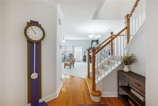 hallway featuring ornamental molding, light wood-style floors, an inviting chandelier, baseboards, and stairs