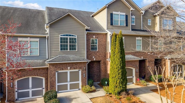 multi unit property with brick siding, roof with shingles, concrete driveway, and an attached garage