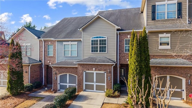 multi unit property featuring brick siding, a garage, concrete driveway, and roof with shingles