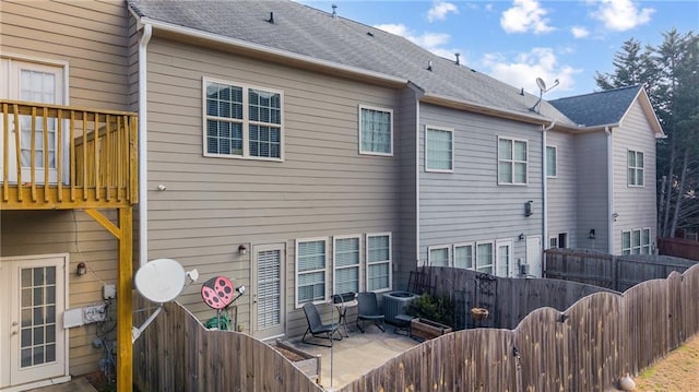 rear view of house with a patio area, cooling unit, a fenced backyard, and roof with shingles