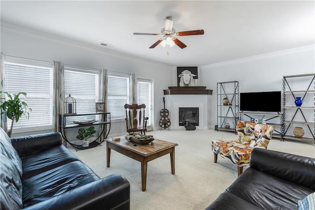 carpeted living room featuring a glass covered fireplace, visible vents, ornamental molding, and ceiling fan