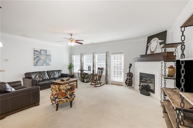 living area featuring a glass covered fireplace, ceiling fan, carpet floors, and ornamental molding