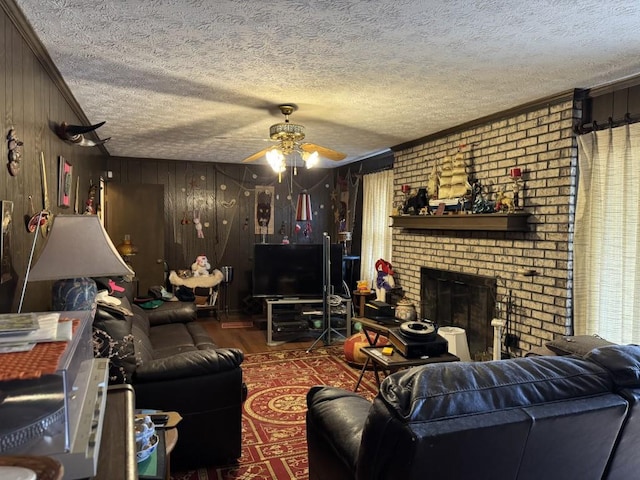 living room featuring wood walls, a brick fireplace, ceiling fan, a textured ceiling, and crown molding