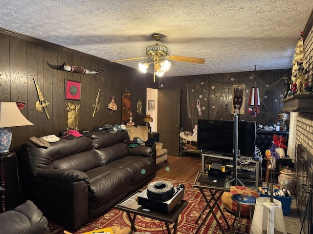 living room with wooden walls, a brick fireplace, ceiling fan, wood-type flooring, and a textured ceiling