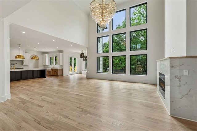 2797 Benson Dr, Marietta, GA 30062 - unfurnished living room with a chandelier, a warm lit fireplace, light wood finished floors, a high ceiling, and recessed lighting
