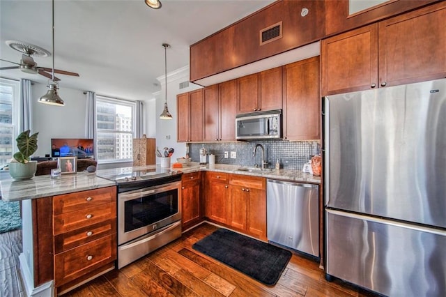 kitchen with decorative backsplash, appliances with stainless steel finishes, decorative light fixtures, a peninsula, and a sink