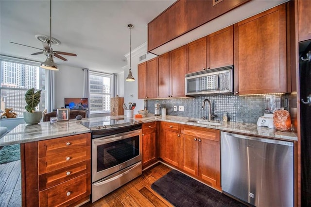 kitchen with stainless steel appliances, brown cabinetry, a peninsula, and a sink