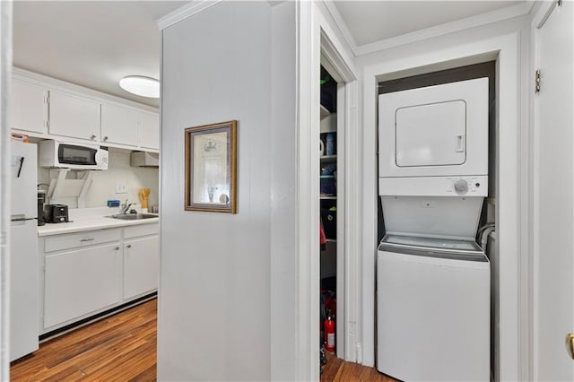 laundry room featuring ornamental molding, a sink, light wood finished floors, and stacked washing maching and dryer