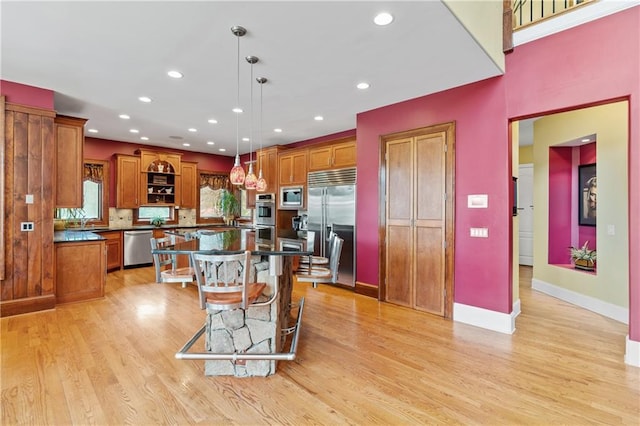 kitchen with a breakfast bar, built in appliances, a kitchen island, decorative light fixtures, and light wood-type flooring