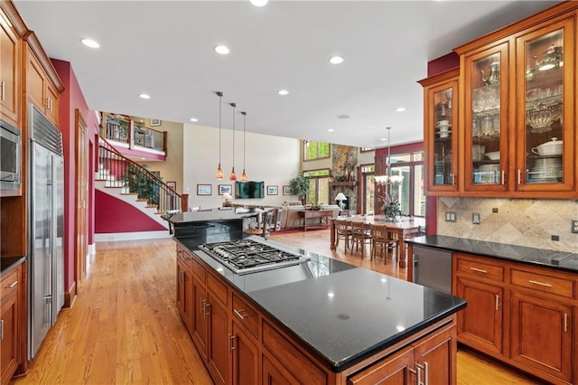 kitchen with a kitchen island, decorative light fixtures, backsplash, built in appliances, and light wood-type flooring