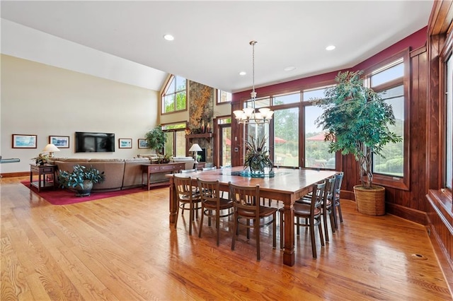 dining area featuring an inviting chandelier, a wealth of natural light, vaulted ceiling, and light wood-type flooring