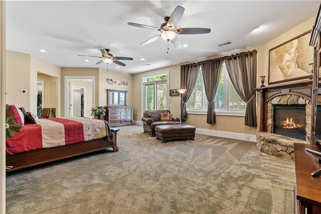 bedroom featuring a stone fireplace, carpet floors, and ceiling fan